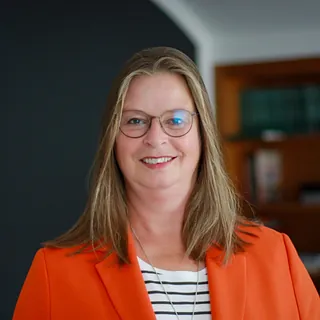 Eine Frau, Dorothea Goudefroy, mit Brille und orangenen Jacket in einem Büro