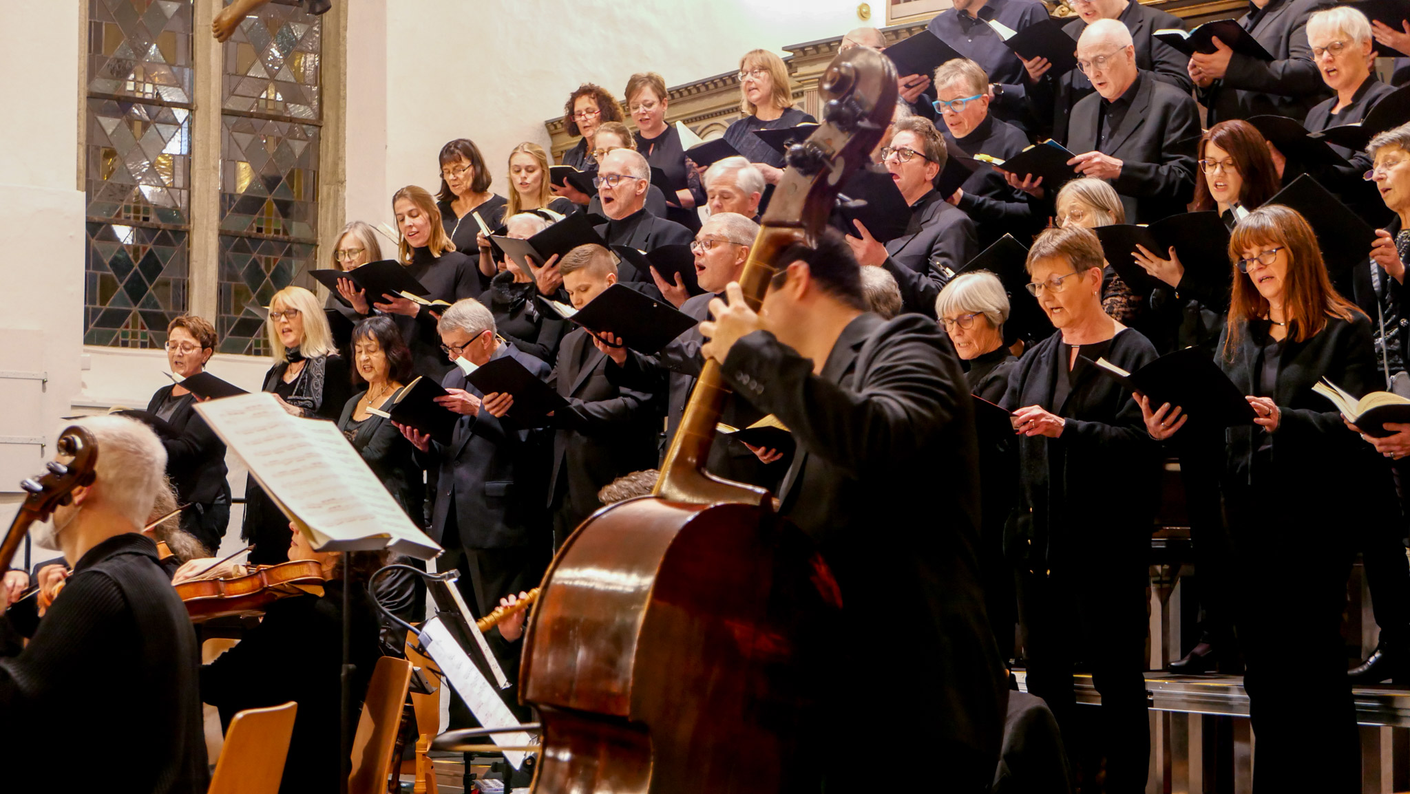 Ein gemischter Chor in Schwarz in einer Kirche, davor ein Orchester, von der Seite gesehen