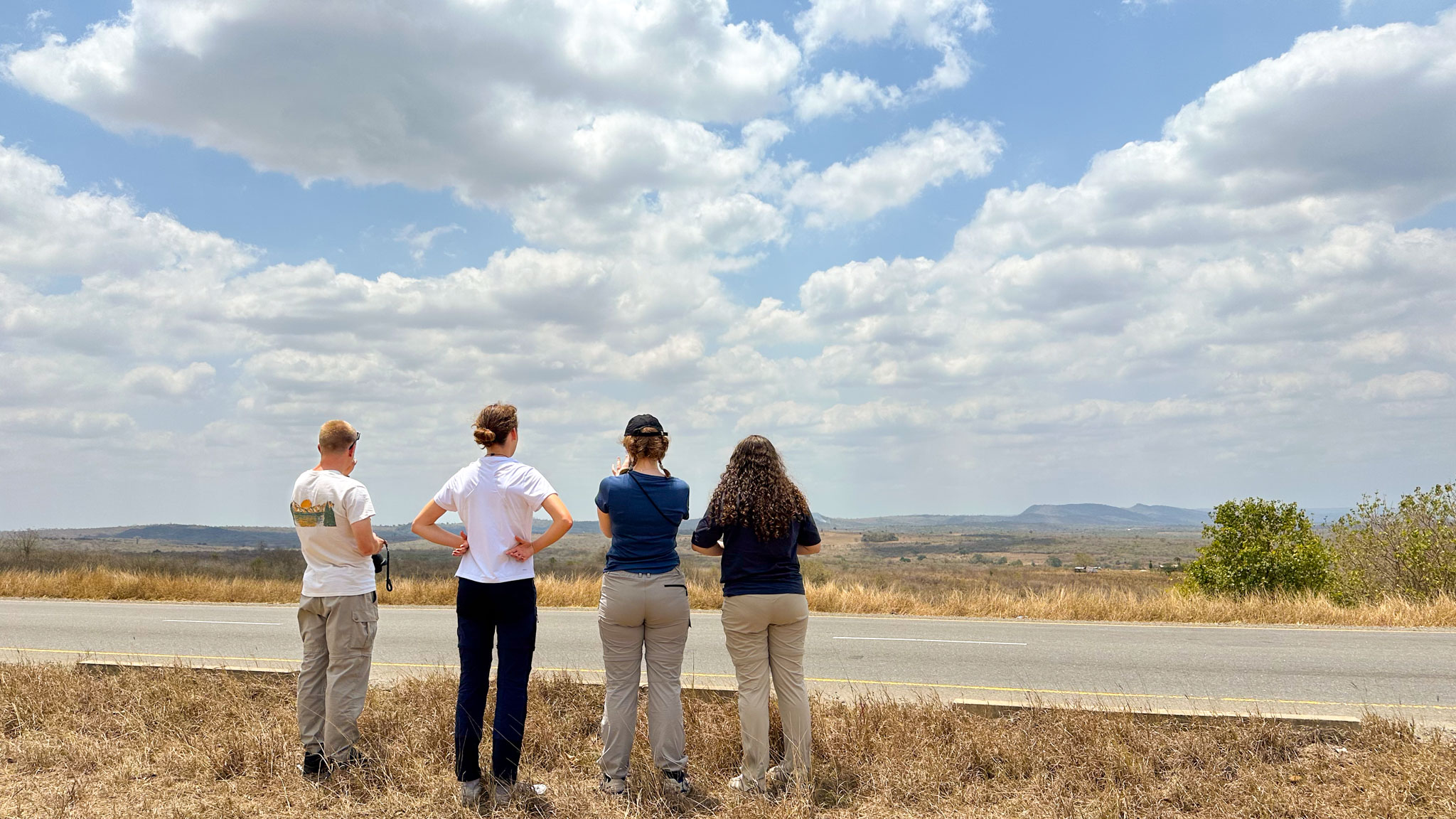Vier Mitglieder der Jugenddelegation am Straßenland in einer Steppenlandschaft schauen, von hinten gesehen, in die Ferne