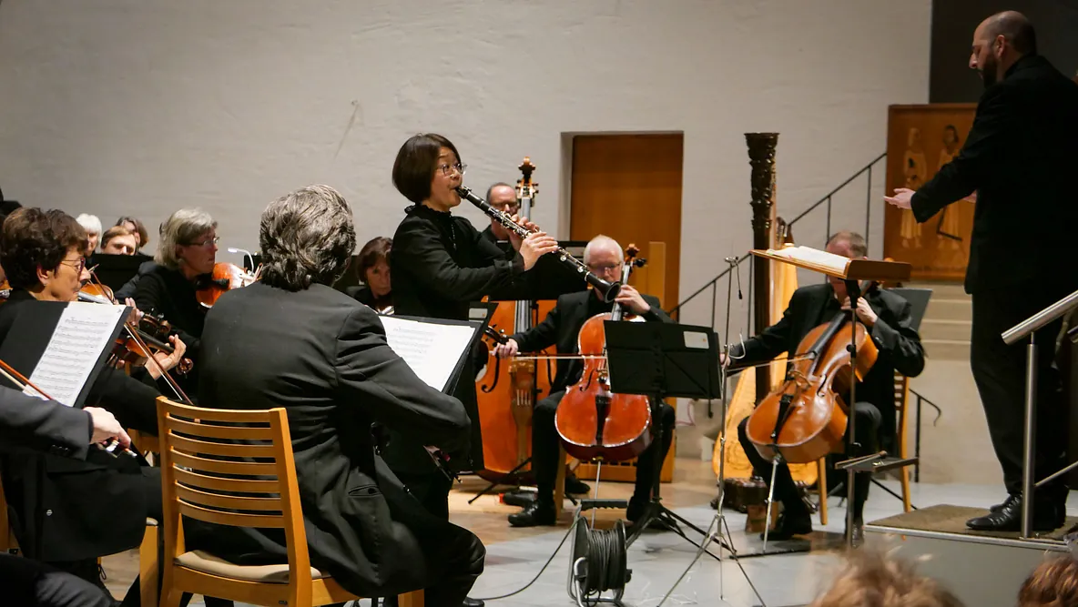 Eine japanische Frau spielt stehend Klarinette in der Mitte eines Orchesters